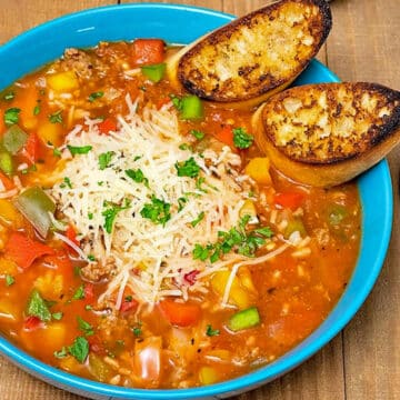 stuffed pepper soup in a blue bowl, with garlic bread on the side of soup bowl