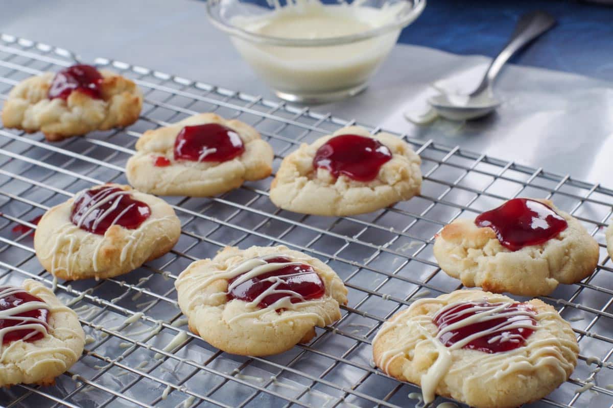 White Chocolate raspberry cookies on a wire cooling rack, being drizzled with white chocolate