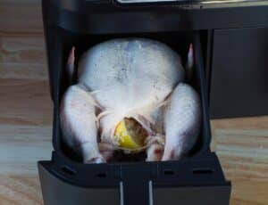 whole chicken in drawer of air fryer with salt and pepper sprinkled on