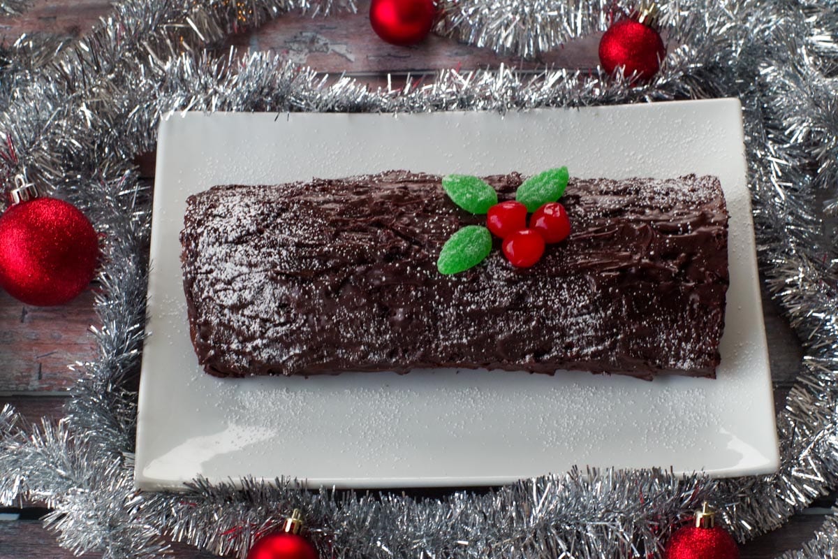 yule log hardened on white platter, garnished with spearmint gummy leaves and maraschino cherries