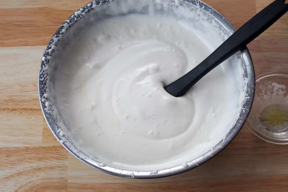 melted butter mixed into egg mixture with a black spatula in bowl and glass bowl on the side