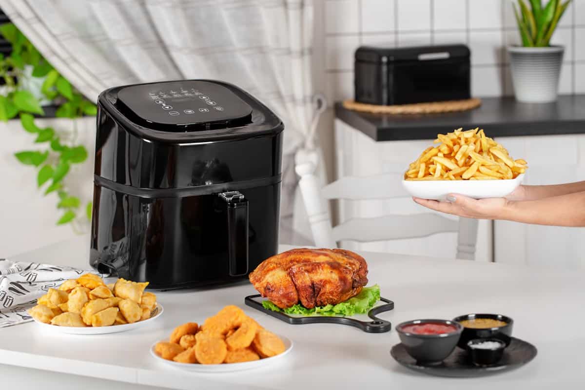 black air fryer surrounded by foods made in the air fryer (fries, wings etc)