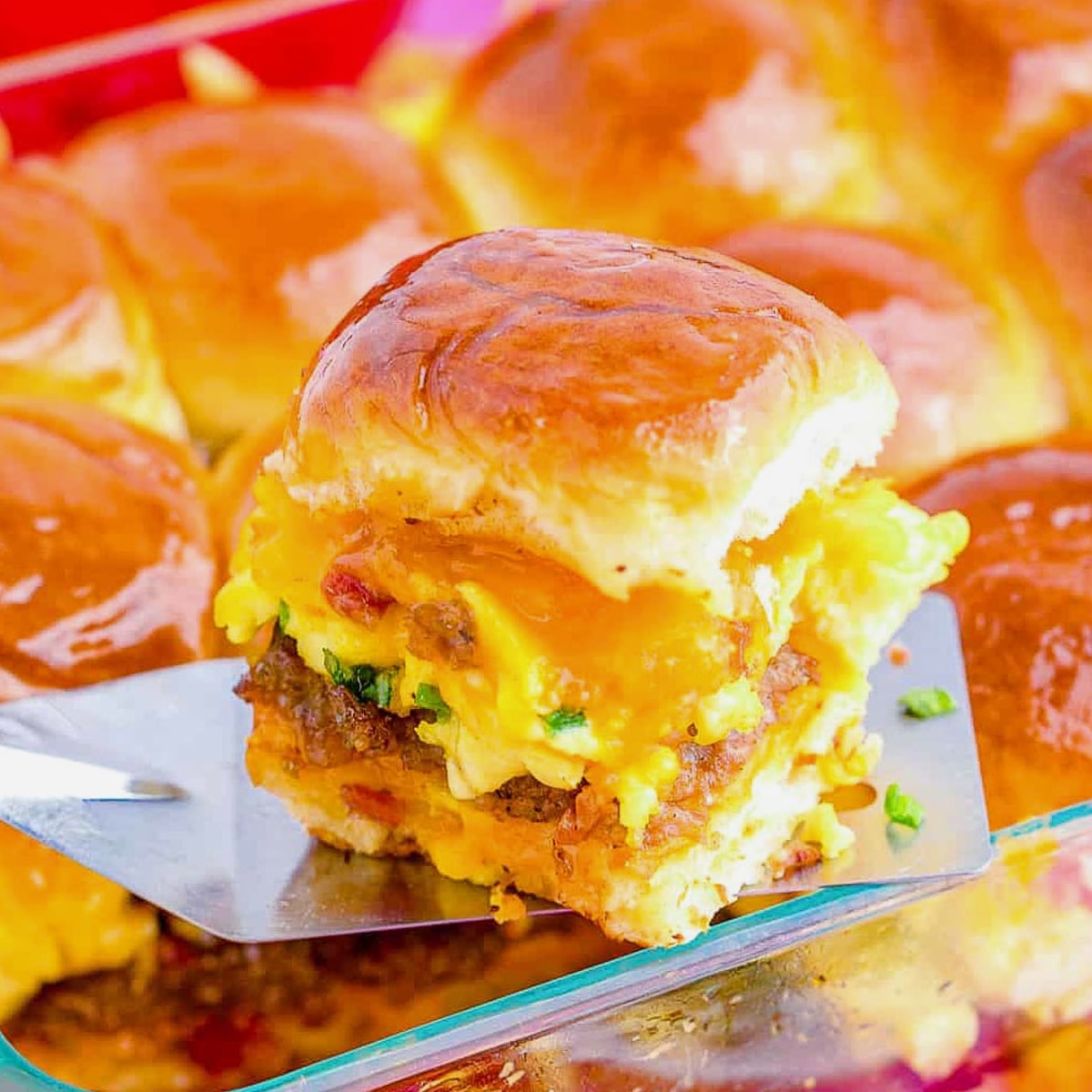 breakfast slider being held up on a spatula over a pan of more sliders