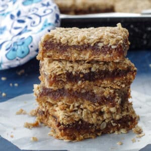 4 date squares piled up on a piece of parchment paper with a blue flowered oven mitt in the background