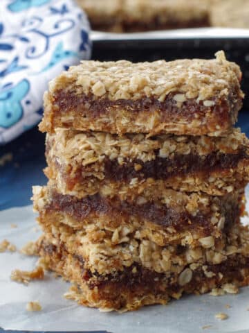 4 date squares piled up on a piece of parchment paper with a blue flowered oven mitt in the background
