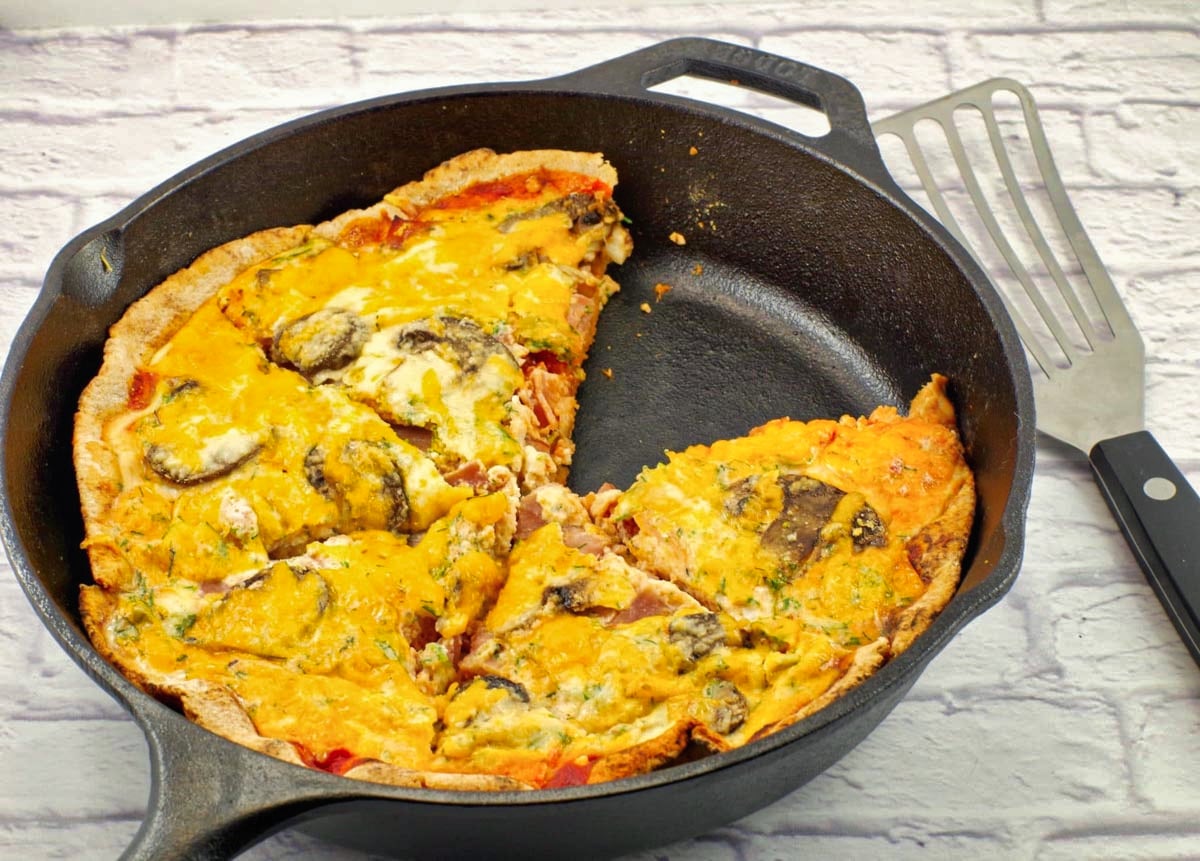 Egg white breakfast pizza in black cast iron frying pan, with piece missing