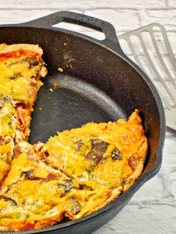 Egg white breakfast pizza in black cast iron frying pan, with piece missing
