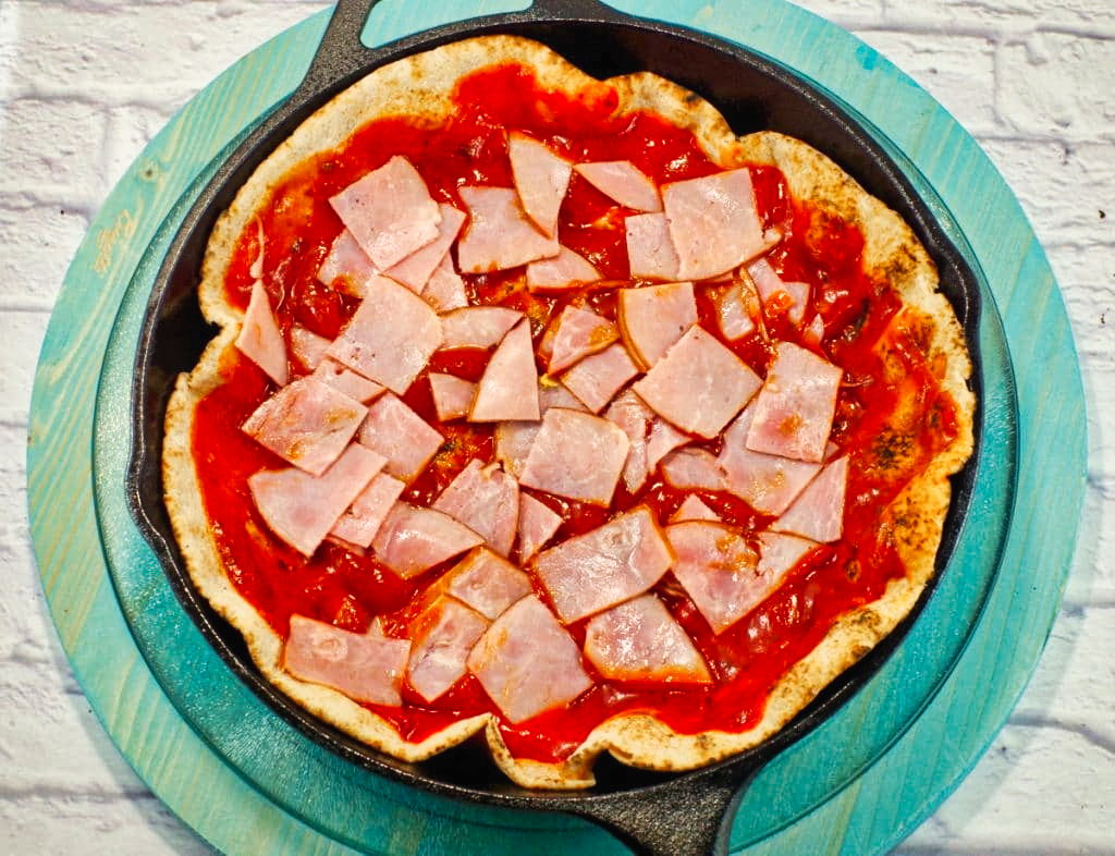 pita bread in a cast iron frying pan with ham and sauce on top