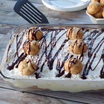 cream puff dessert in a glass dish with plates and a bowl of cream puffs in background