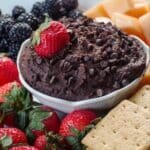 Dark Chocolate Hummus in a white petal bowl, with a strawberry in the hummus, on a platter of fruit and graham crackers