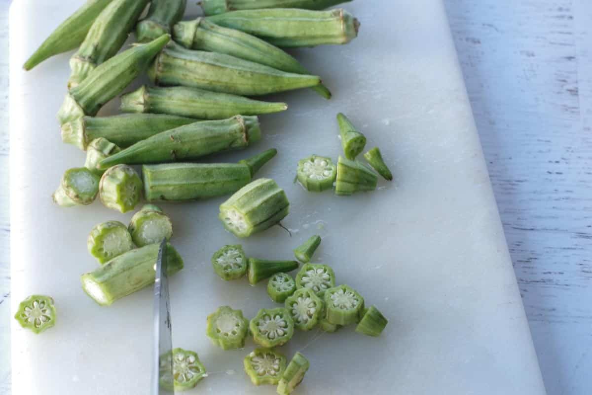 okra being sliced on a white cutting board