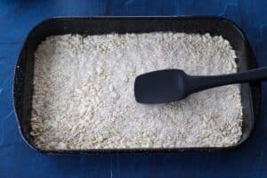 flour and oat mixture being pressed into the bottom of a pan with spatula