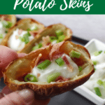air fryer potato skin being held up over a tray of more air fryer potato skins
