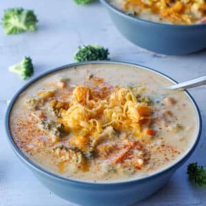 broccoli cheese soup in a blue bowl with a spoon, with broccoli scattered around