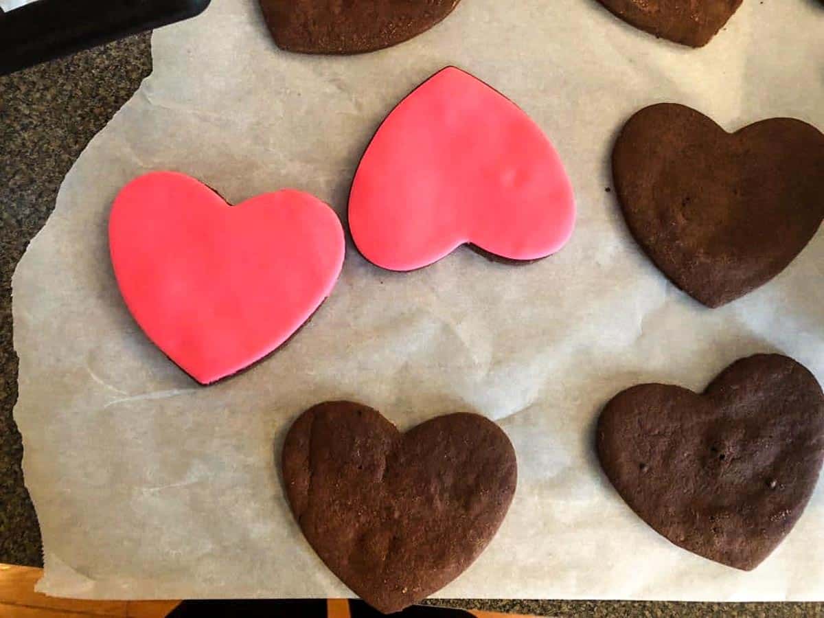 chocolate heart cookies being covered in pink fondant heart shapes
