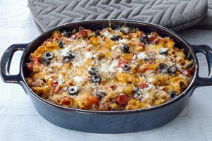 healthy pizza casserole in a blue casserole dish with grey oven mitts in the background