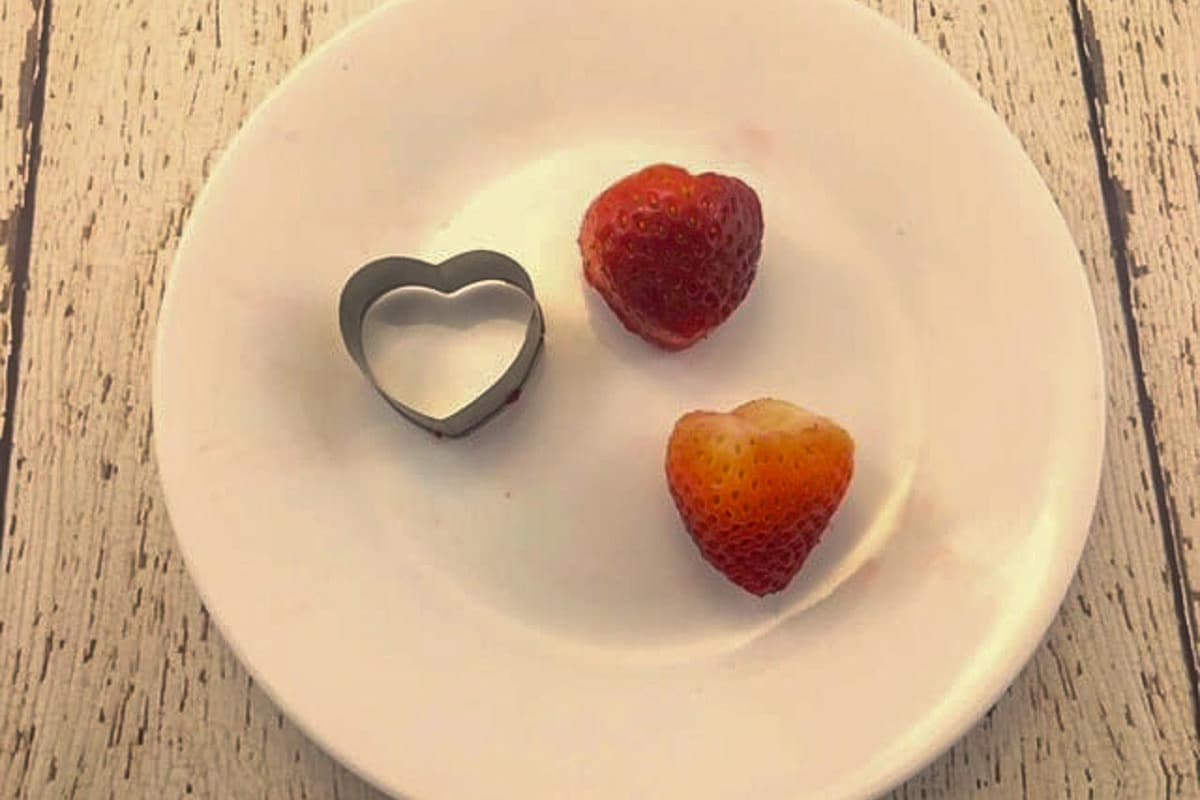 strawberries being cut into heart shapes with small heart-shaped cookie cutter