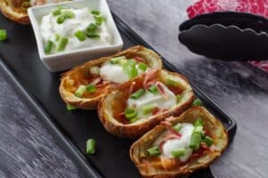 3 air fryer potato skins on a black platter with a white dish of sour cream in the middle