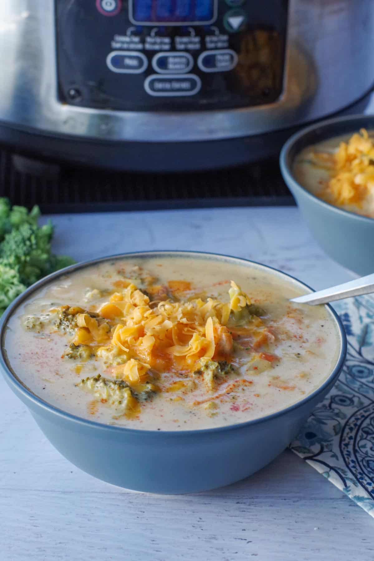 slow cooker broccoli cheese soup in a blue bowl in front of a slow cooker