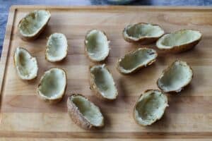 half potatoes with insides scooped out, on a wooden cutting board