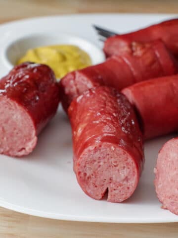 several pieces of kielbasa on a white plate with a small white dish of mustard