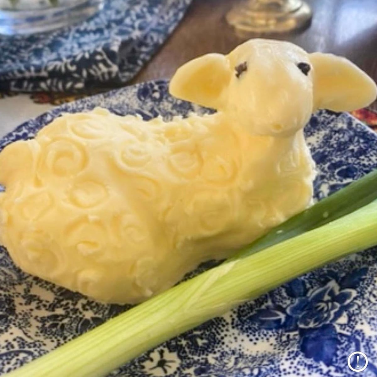 lamb carved out of butter on blue floral patterned material with slice of green onion in front