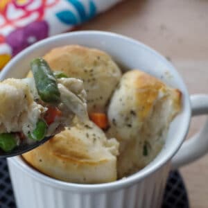 personal chicken pot pie in a white meal mug, with a bit being held up on a spoon