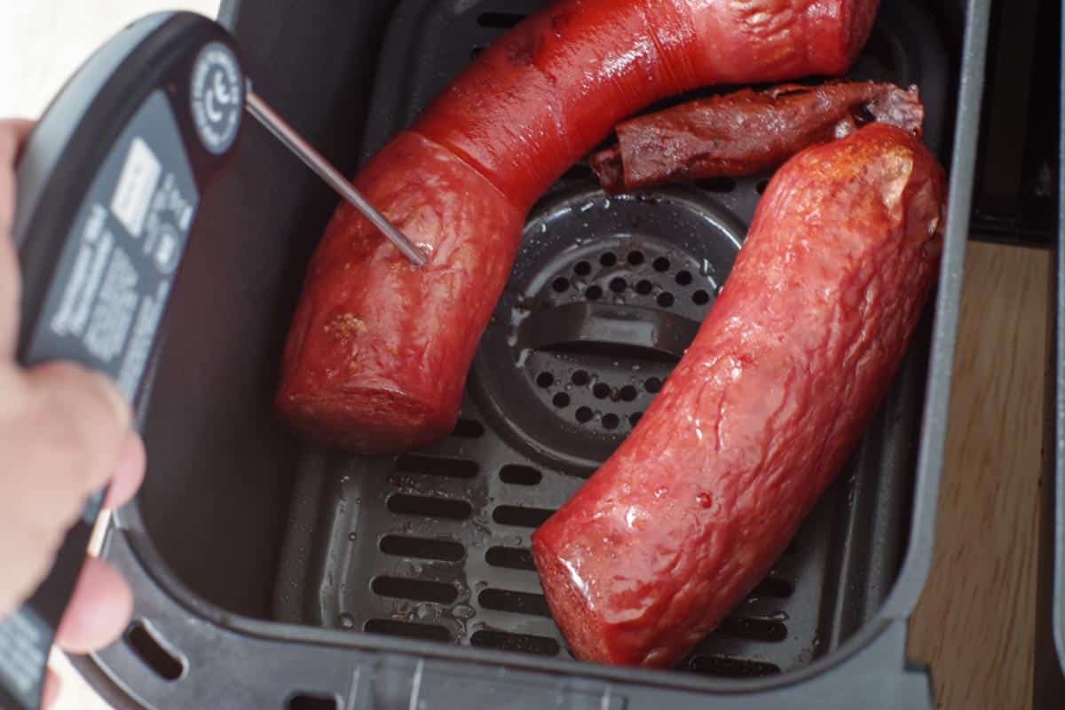 kielbasa in air fryer drawer with an instant read thermometer taking internal temperature