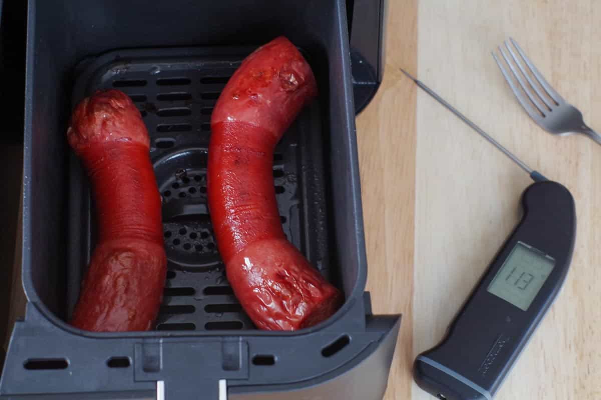 cooked kielbasa in the drawer of an air fryer with a black instant read thermometer to the right