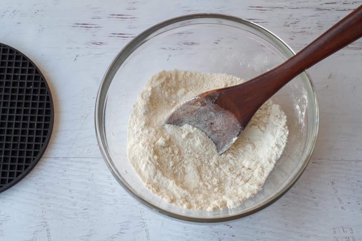 flour and sugar mixed together in a glass mixing bowl, with wooden spoon