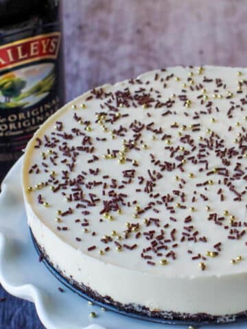 Whole No bake Baileys cheesecake on a white cake platter with a bottle of baileys in the background