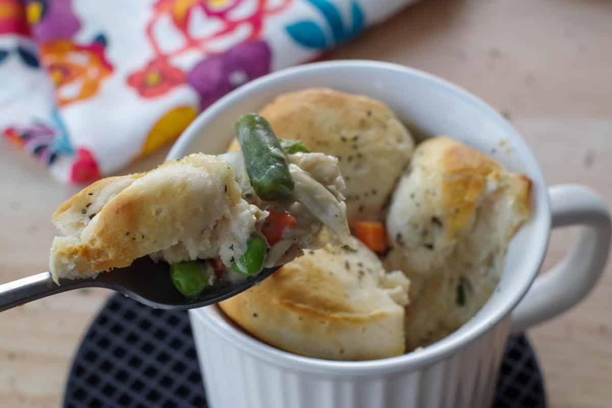 personal chicken pot pie in a white meal mug, with a bit being held up on a spoon