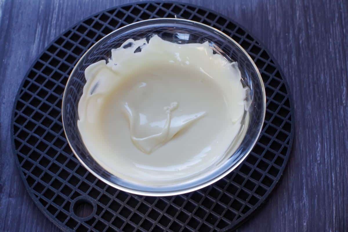 melted white chocolate in a glass bowl on a black silicone trivet