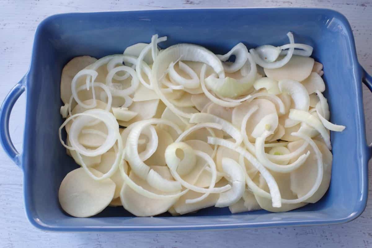 sliced potatoes and onions on bottom of blue casserole dish
