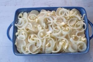 final layer of potatoes, onions, butter and salt and pepper with milk poured over top, in a blue casserole dish