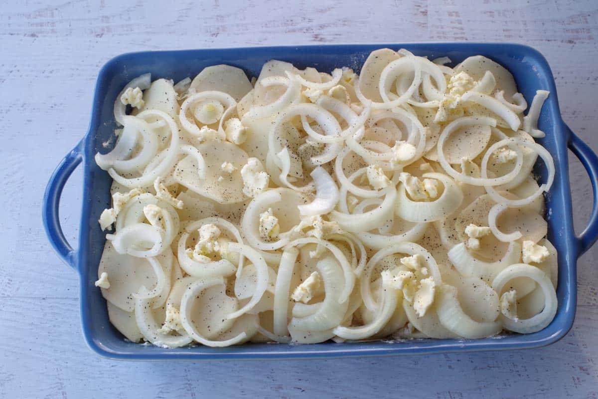 final layer of potatoes, onions, butter and salt and pepper with milk poured over top, in a blue casserole dish