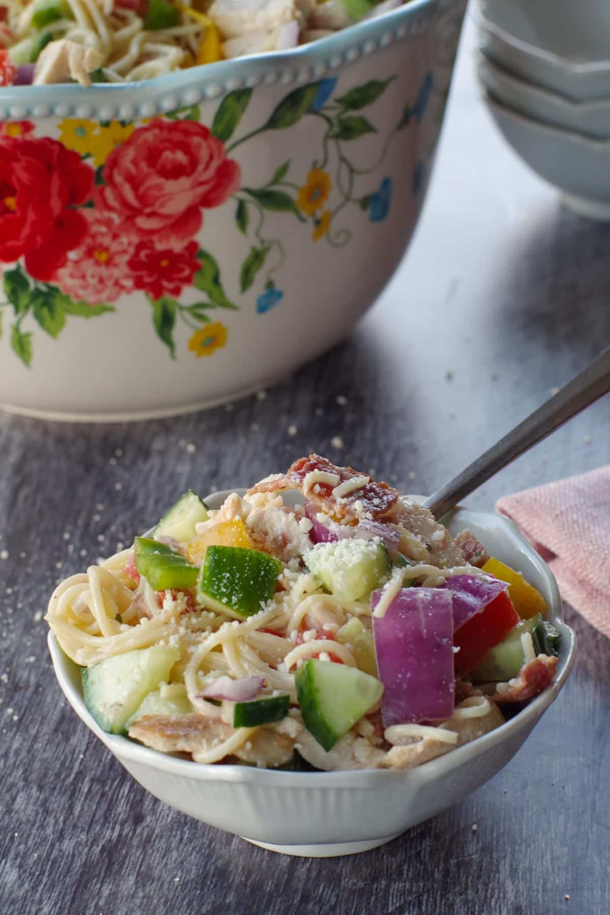 chicken bacon ranch pasta salad in a small white bowl, with a fork and a large bowl of salad in background