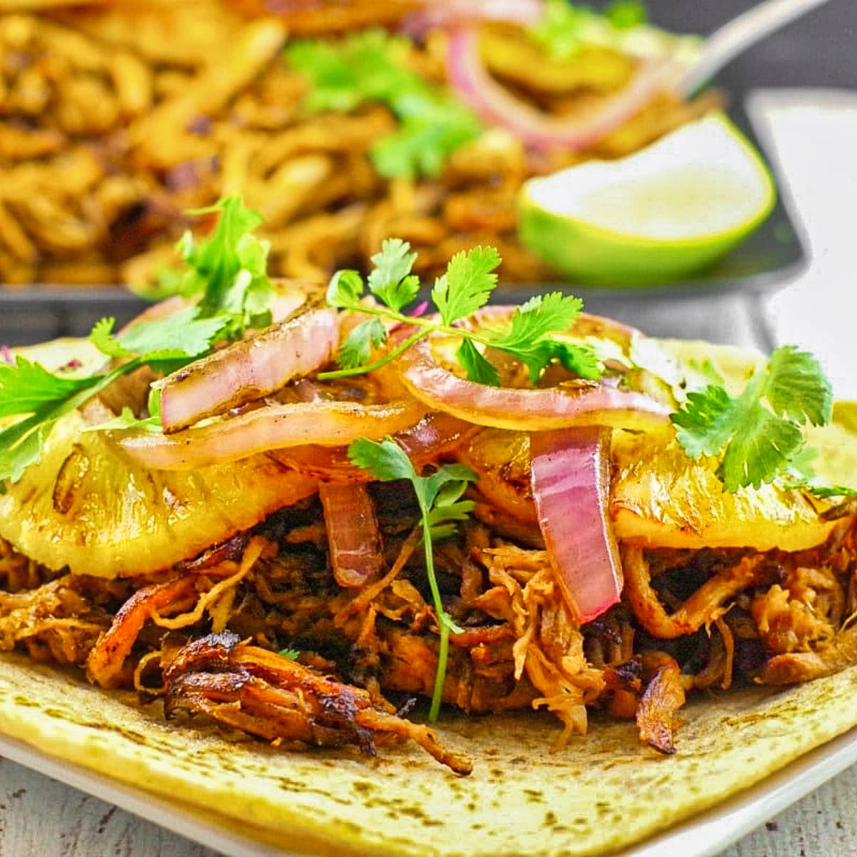 pineapple carnita on a soft taco shell with a tray of carnitas in background