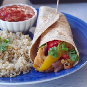 air fryer fajitas in a wrap, on a blue plate with rice, salsa and a wedge of lime