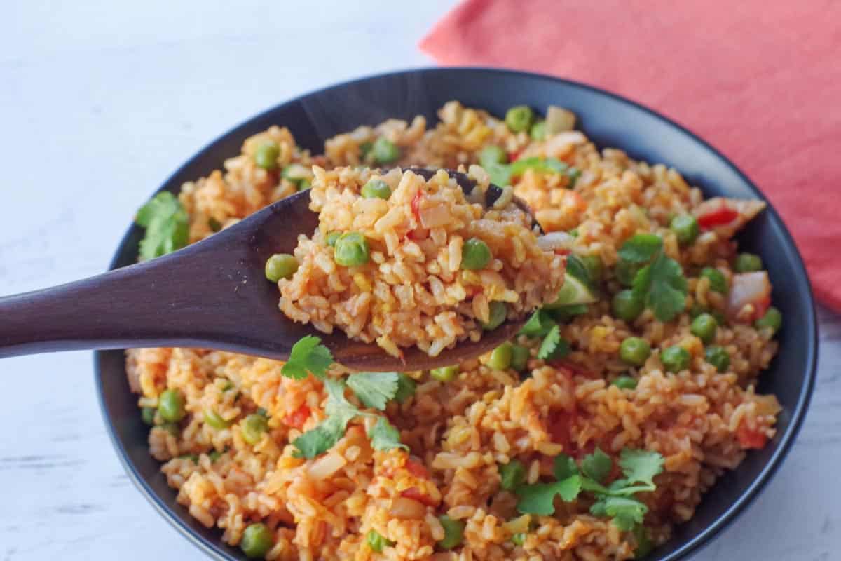 Spanish brown rice in a black bowl, with a spoonful being held up on a wooden spoon