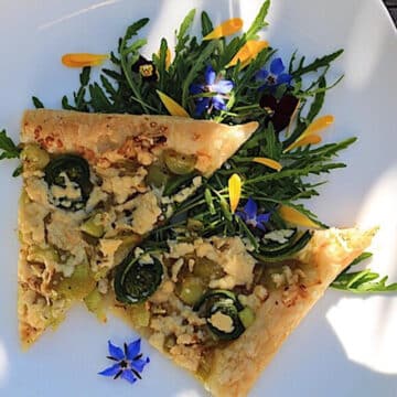 2 slices of fiddlehead tart of a white plate, over salad
