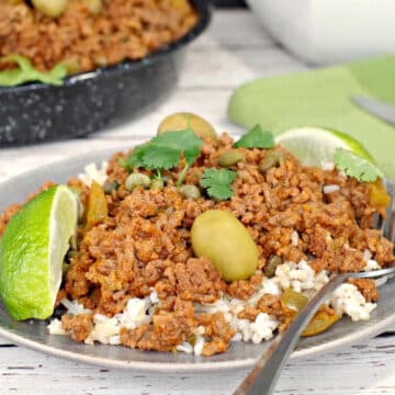 healthy picadillo over rice, on a plate with a fork and pan of more picadillo in the background