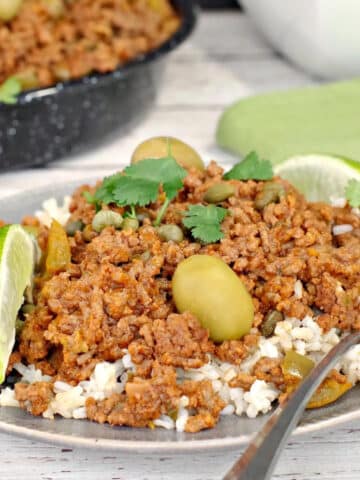 healthy picadillo over rice, on a plate with a fork and pan of more picadillo in the background