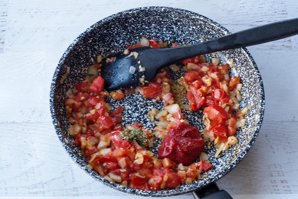 tomato paste and spices added to the skillet, with black spatula