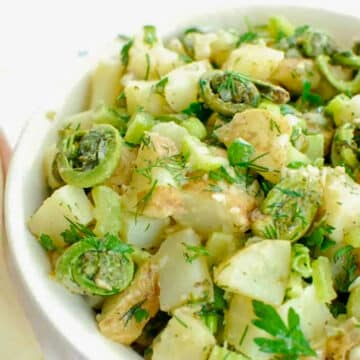 Vegan potato salad with fiddleheads in a white bowl