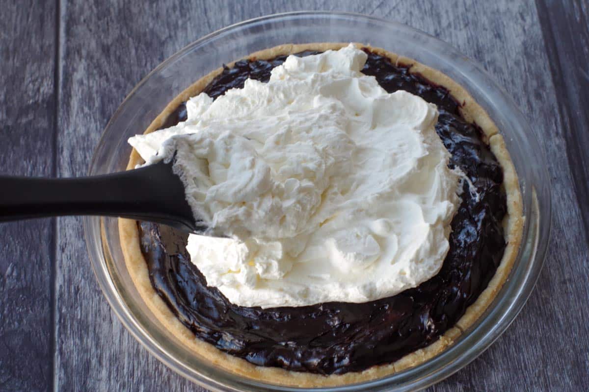 whipped cream being spread onto chocolate pie