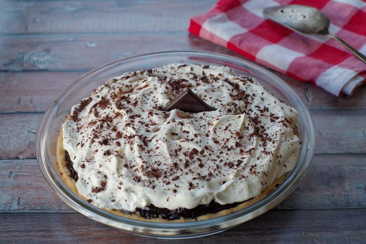 chocolate pie in a glass pie dish with red and white checkered towel in the background