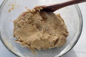 rhubarb cookie dough in a glass bowl with a dark brown wooden spoon