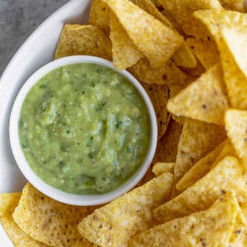 salsa verde in a small white bowl, on white platter, surrounded by nacho chips