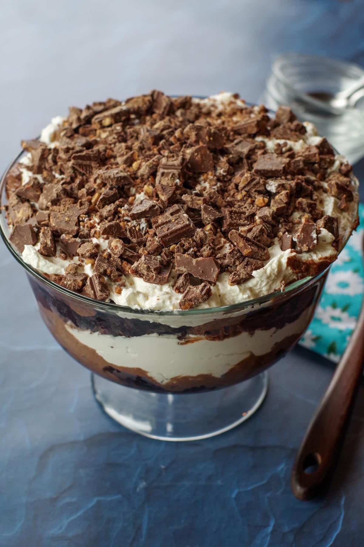 death by chocolate trifle on a blue surface with small glass bowls in the background and a tea towel with a wooden spoon on the side
